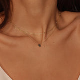 a black Hamsa hand charm necklace in 18k gold plated silver. The necklace features a delicate chain with a beautifully designed Hamsa hand charm pendant. The Hamsa hand symbol is believed to bring protection, good luck, and ward off evil. The necklace is designed to be worn comfortably and can be adjusted to fit different neck sizes.