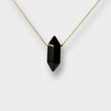 Black obsidian crystal necklace. The necklace features a pointed black obsidian crystal pendant attached to a gold chain, creating a stunning and eye-catching piece of jewelry.