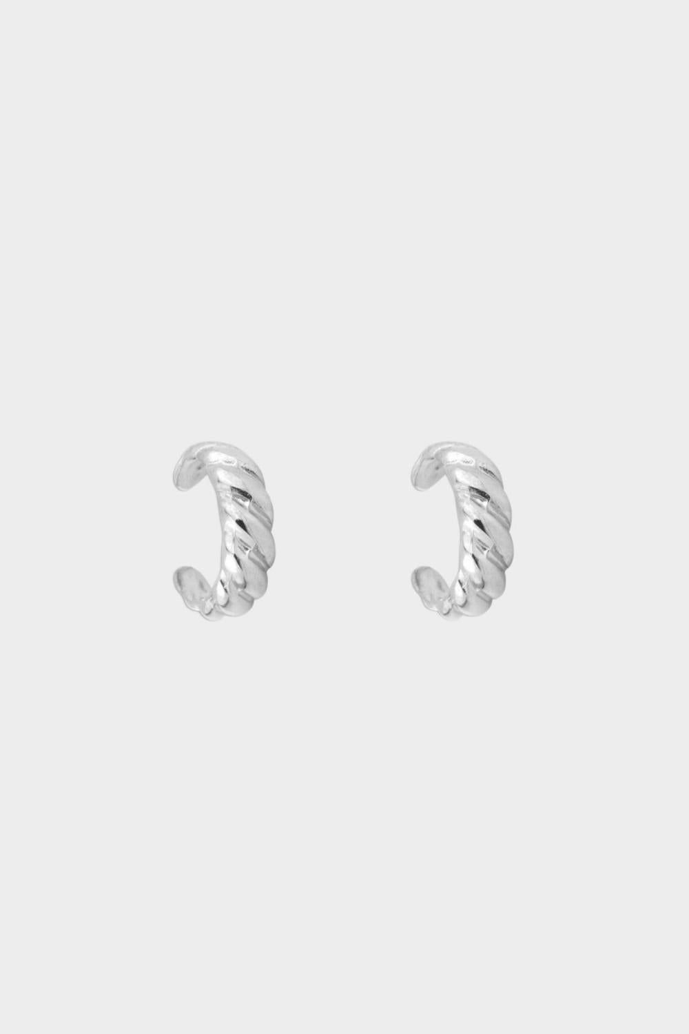 a croissant ear cuff in sterling silver. The ear cuff features a unique croissant-shaped design that wraps around the earlobe. It is made of high-quality silver with a polished finish, giving it a luxurious and elegant look. The cuff is designed to be worn without the need for a piercing, making it a trendy and versatile accessory.