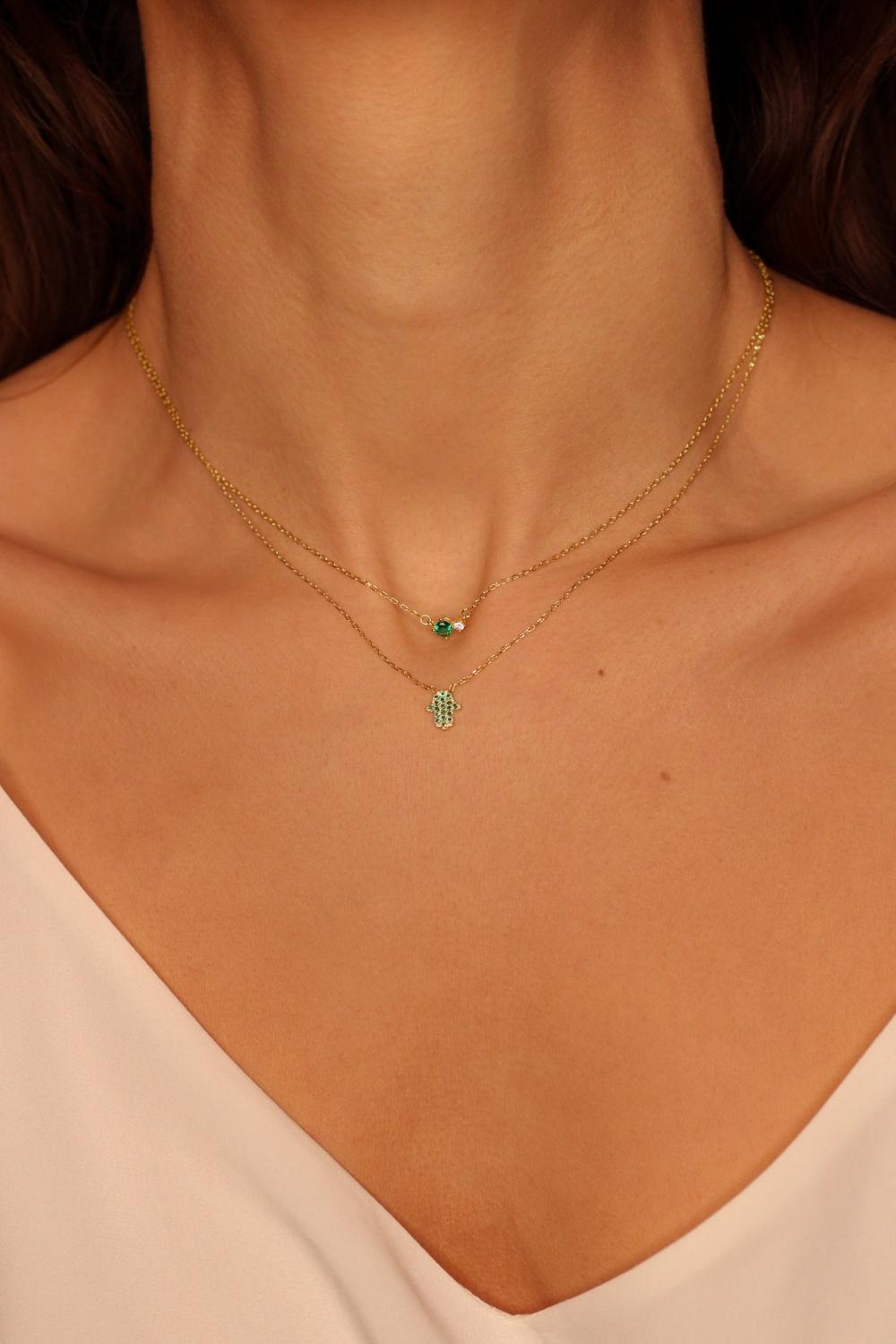 A Green Hamsa hand charm necklace in 18k gold plated silver. The necklace features a delicate chain with a beautifully designed Hamsa hand charm pendant. The Hamsa hand symbol is believed to bring protection, good luck, and ward off evil. The necklace is designed to be worn comfortably and can be adjusted to fit different neck sizes.