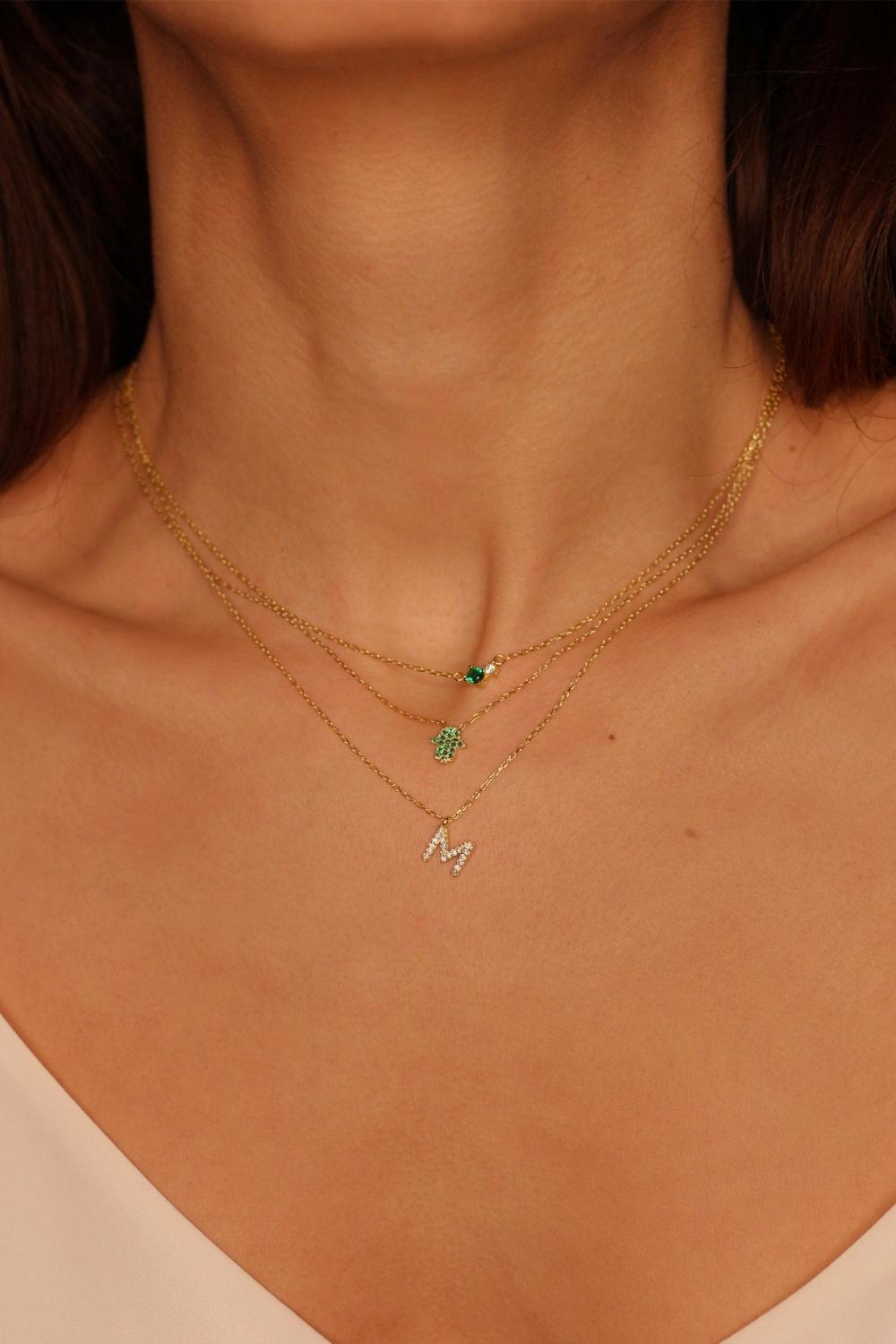 A Green Hamsa hand charm necklace in 18k gold plated silver. The necklace features a delicate chain with a beautifully designed Hamsa hand charm pendant. The Hamsa hand symbol is believed to bring protection, good luck, and ward off evil. The necklace is designed to be worn comfortably and can be adjusted to fit different neck sizes.