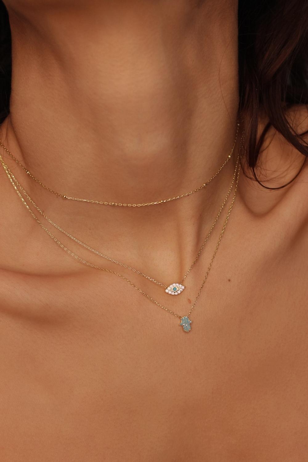 A blue Hamsa hand charm necklace in 18k gold plated silver. The necklace features a delicate chain with a beautifully designed Hamsa hand charm pendant. The Hamsa hand symbol is believed to bring protection, good luck, and ward off evil. The necklace is designed to be worn comfortably and can be adjusted to fit different neck sizes.