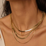 A layered set of herringbone flat chains in 18k gold plated. The set includes multiple flat chains with a distinct herringbone pattern, all crafted in a luxurious gold color. The chains are layered together, creating a stylish and modern look. The herringbone pattern adds a unique texture and visual interest to the chains, while the gold color adds a touch of glamour