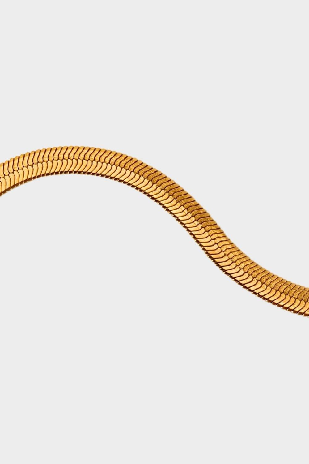 A detail of herringbone flat chain in 18k gold plated. The chain features a distinct herringbone pattern with flat, interlocking links that create a sleek and polished appearance. The gold color adds a touch of luxury and elegance to the chain. The herringbone flat chain is a versatile accessory that can be worn on its own as a statement piece or layered with other necklaces for a stylish and trendy look. This chain is perfect for both casual and formal occasions, adding a touch of glamour to any outfit.