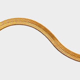 A detail of herringbone flat chain in 18k gold plated. The chain features a distinct herringbone pattern with flat, interlocking links that create a sleek and polished appearance. The gold color adds a touch of luxury and elegance to the chain. The herringbone flat chain is a versatile accessory that can be worn on its own as a statement piece or layered with other necklaces for a stylish and trendy look. This chain is perfect for both casual and formal occasions, adding a touch of glamour to any outfit.