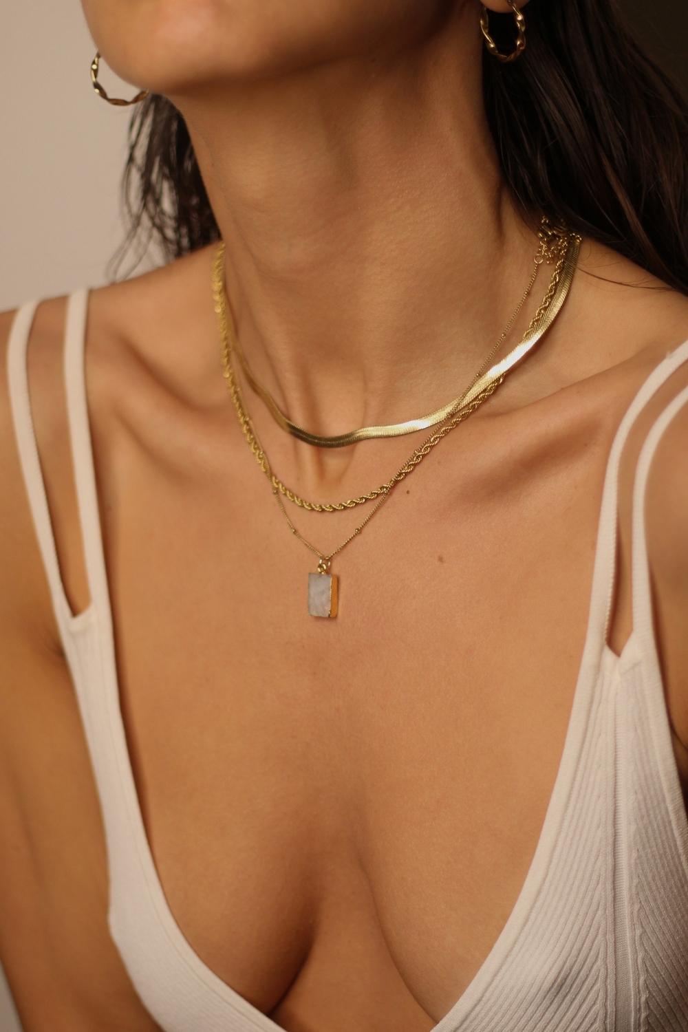 A layered set of herringbone flat chains in 18k gold plated. The set includes three gold chains with a distinct herringbone pattern, all crafted in a luxurious gold color. The chains are layered together, creating a stylish and modern look. The herringbone pattern adds a unique texture and visual interest to the chains, while the gold color adds a touch of glamour