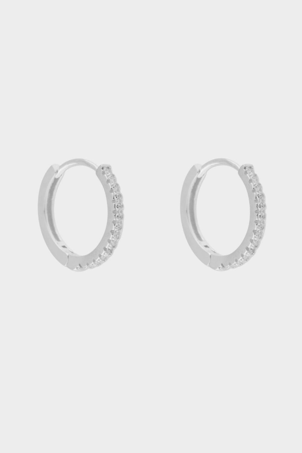 diamond huggie hoops in sterling silver. The earrings feature a classic huggie-style design adorned with sparkling diamonds. The diamonds are meticulously set along the front of the hoops, adding a touch of luxury and glamour. The hoops are made of high-quality silver and have a polished finish.