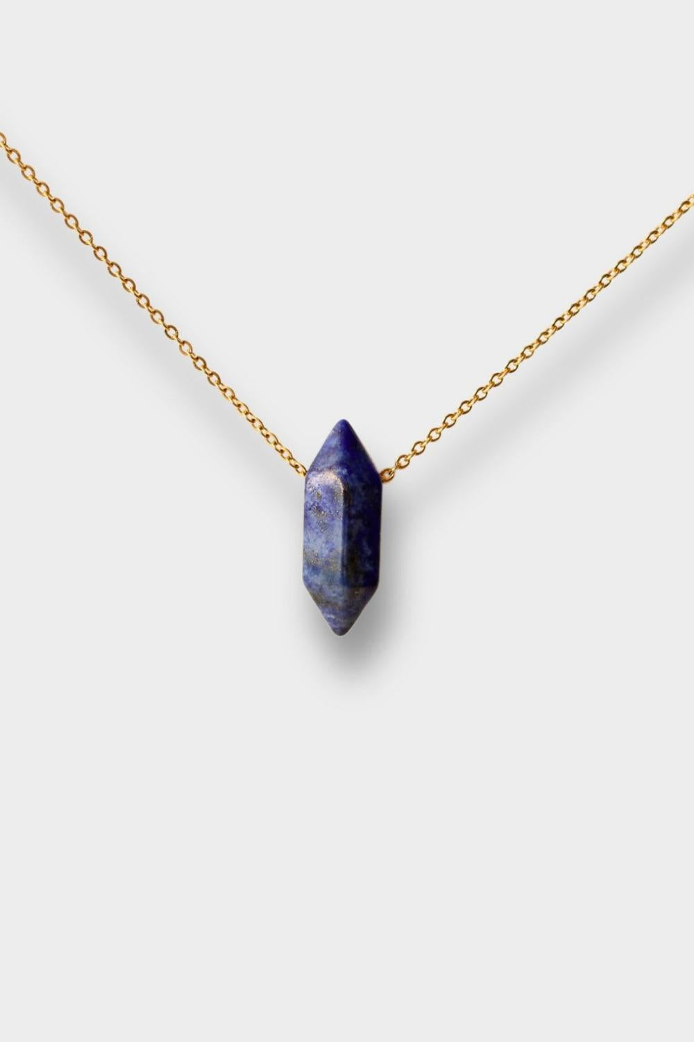 Natural Lapis lazuli crystal necklace. The necklace features a pointed lapis lazuli crystal pendant with a deep blue color and golden flecks. The crystal is attached to a gold chain, creating a stunning and eye-catching piece of jewelry.