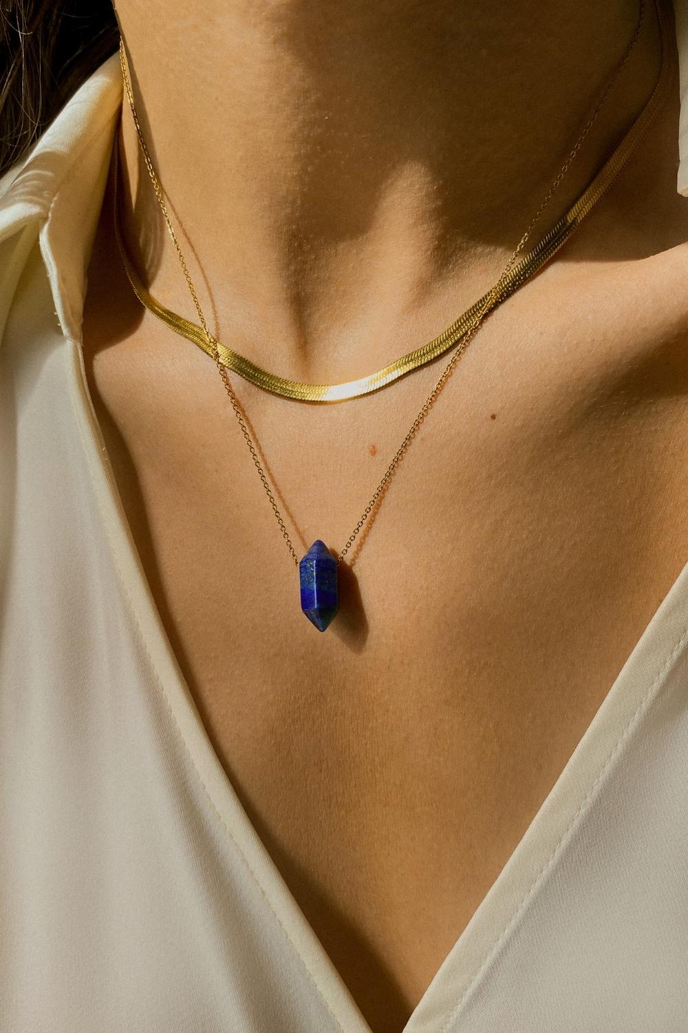 Lapis lazuli crystal necklace. The first necklace features a pointed lapis lazuli crystal pendant, while the second necklace features a delicate gold snake chain. Together, the necklaces create a stunning layered look that adds sophistication and elegance to any outfit.