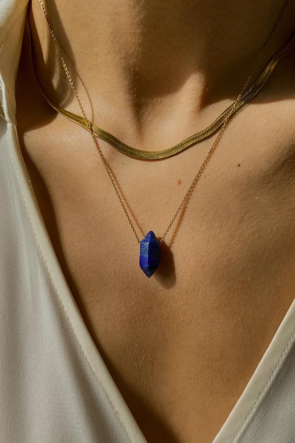 Lapis lazuli crystal necklace. The first necklace features a pointed lapis lazuli crystal pendant, while the second necklace features a delicate gold snake chain. Together, the necklaces create a stunning layered look that adds sophistication and elegance to any outfit.