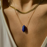 Lapis lazuli crystal necklace. The first necklace features a pointed lapis lazuli crystal pendant, while the second necklace features a delicate gold snake chain. Together, the necklaces create a stunning layered look that adds sophistication and elegance to any outfit.