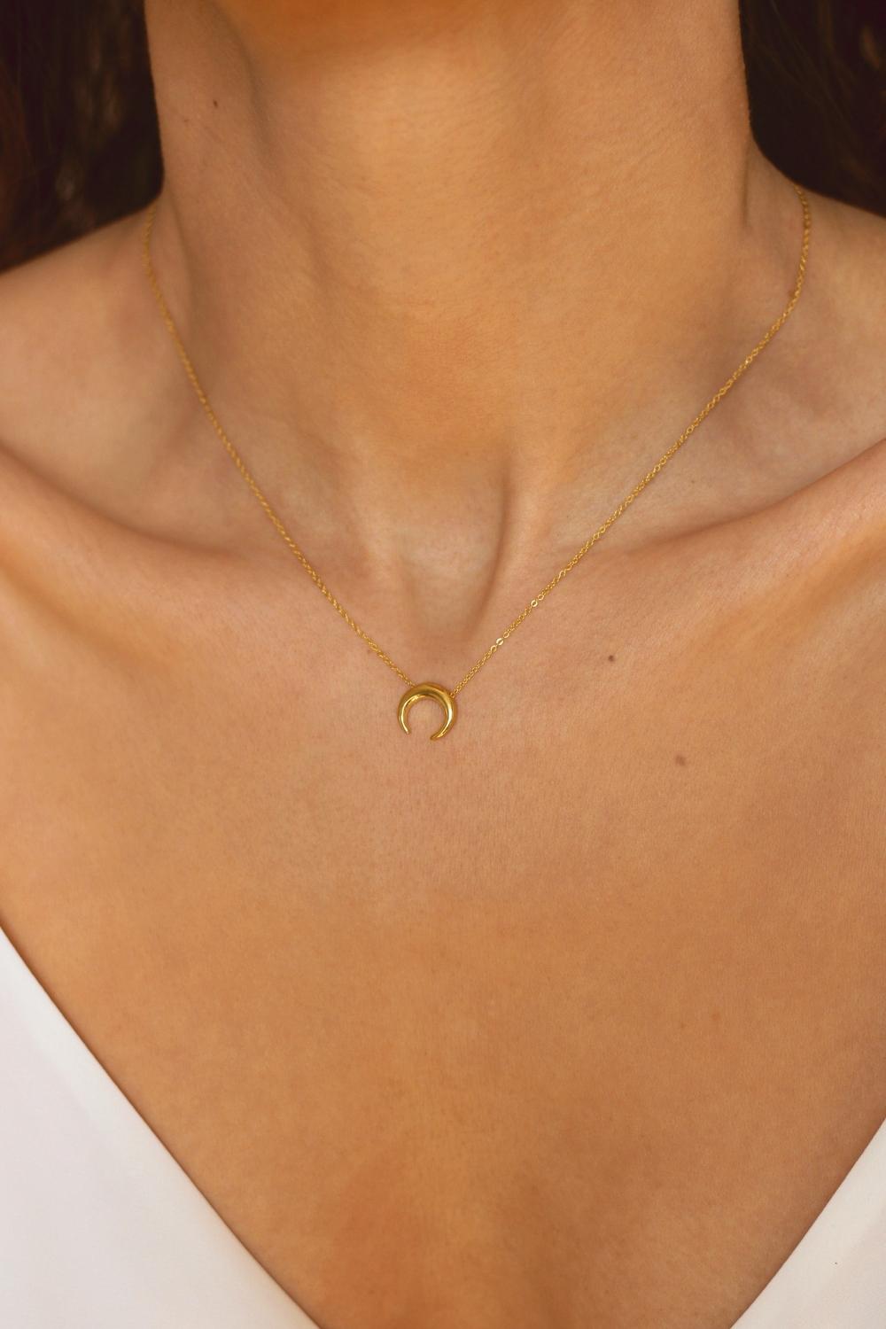 A moon necklace in 18k gold plated silver. The necklace features a delicate gold chain with a pendant in the shape of a crescent moon. The necklace is perfect for those who love celestial-inspired jewelry, and makes for an elegant and stylish accessory that can be worn on any occasion.
