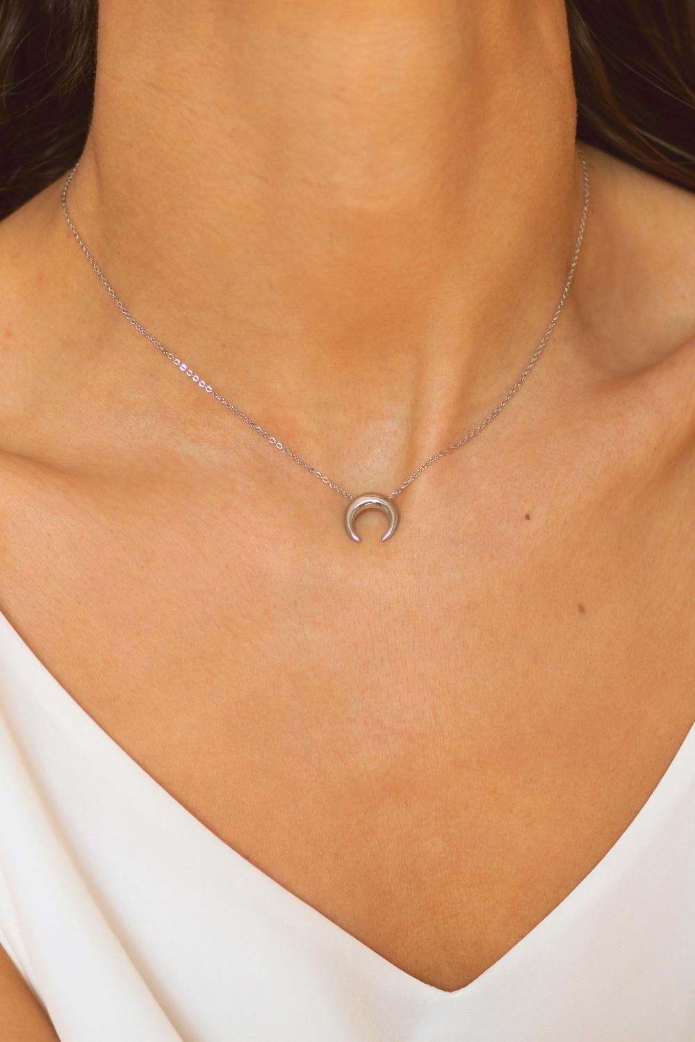 A moon necklace in sterling silver. The necklace features a delicate silver chain with a pendant in the shape of a crescent moon. The necklace is perfect for those who love celestial-inspired jewelry, and makes for an elegant and stylish accessory that can be worn on any occasion.
