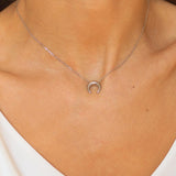 A moon necklace in sterling silver. The necklace features a delicate silver chain with a pendant in the shape of a crescent moon. The necklace is perfect for those who love celestial-inspired jewelry, and makes for an elegant and stylish accessory that can be worn on any occasion.