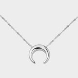 A moon necklace in sterling silver. The necklace features a delicate silver chain with a pendant in the shape of a crescent moon. The necklace is perfect for those who love celestial-inspired jewelry, and makes for an elegant and stylish accessory that can be worn on any occasion.