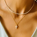 A layered pearl necklace set, featuring a pearl cross pendant necklace and a beaded pearl choker. The pearl cross pendant necklace is crafted from delicate gold-plated silver and features a cross pendant adorned with lustrous white pearls. The necklace is layered with a beaded pearl choker, which features delicate gold chains and lustrous white pearls threaded onto the chains.