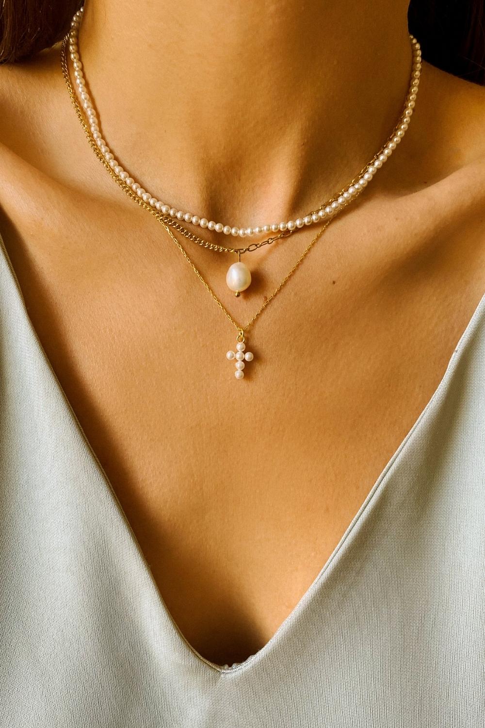 A layered pearl necklace set, featuring a pearl cross pendant necklace, single pearl necklace and a beaded pearl choker. The pearl cross pendant necklace is crafted from delicate 18k gold-plated silver and features a cross pendant adorned with lustrous white pearls. The necklace is layered with a beaded pearl choker, which features delicate gold chains and lustrous white pearls threaded onto the chains.