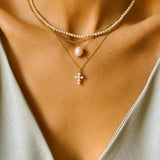 A layered pearl necklace set, featuring a pearl cross pendant necklace, single pearl necklace and a beaded pearl choker. The pearl cross pendant necklace is crafted from delicate 18k gold-plated silver and features a cross pendant adorned with lustrous white pearls. The necklace is layered with a beaded pearl choker, which features delicate gold chains and lustrous white pearls threaded onto the chains.