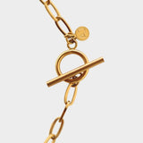 18k gold plated toggle choker necklace. The necklace features a sleek and minimalistic design, with a single chain crafted from high-quality metal and plated with 18k gold for a luxurious finish. The centerpiece of the necklace is a toggle closure, consisting of a small, decorative gold ring and a bar that fits through it to secure the necklace. This chic and elegant accessory adds a touch of sophistication to any outfit