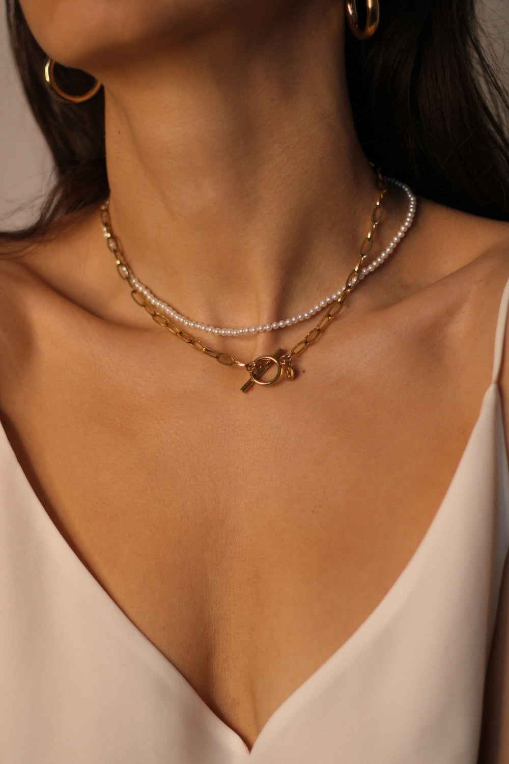 Waterproof 18k gold plated toggle choker. The set includes a sleek and minimalistic 18k gold plated toggle choker with a decorative gold ring and a bar that fits through it to secure the necklace. The choker is layered with a beaded pearl necklace, featuring lustrous white pearls strung on a delicate gold chain. The two necklaces complement each other perfectly, adding a touch of elegance and sophistication to the model's outfit