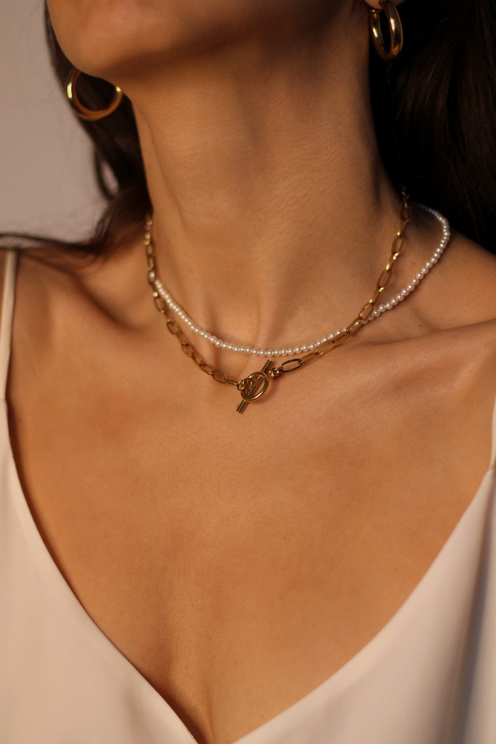 Waterproof 18k gold plated toggle choker.The set includes a sleek and minimalistic 18k gold plated toggle choker with a decorative gold ring and a bar that fits through it to secure the necklace. The choker is layered with a beaded pearl necklace, featuring lustrous white pearls strung on a delicate gold chain. The two necklaces complement each other perfectly, adding a touch of elegance and sophistication to the model's outfit