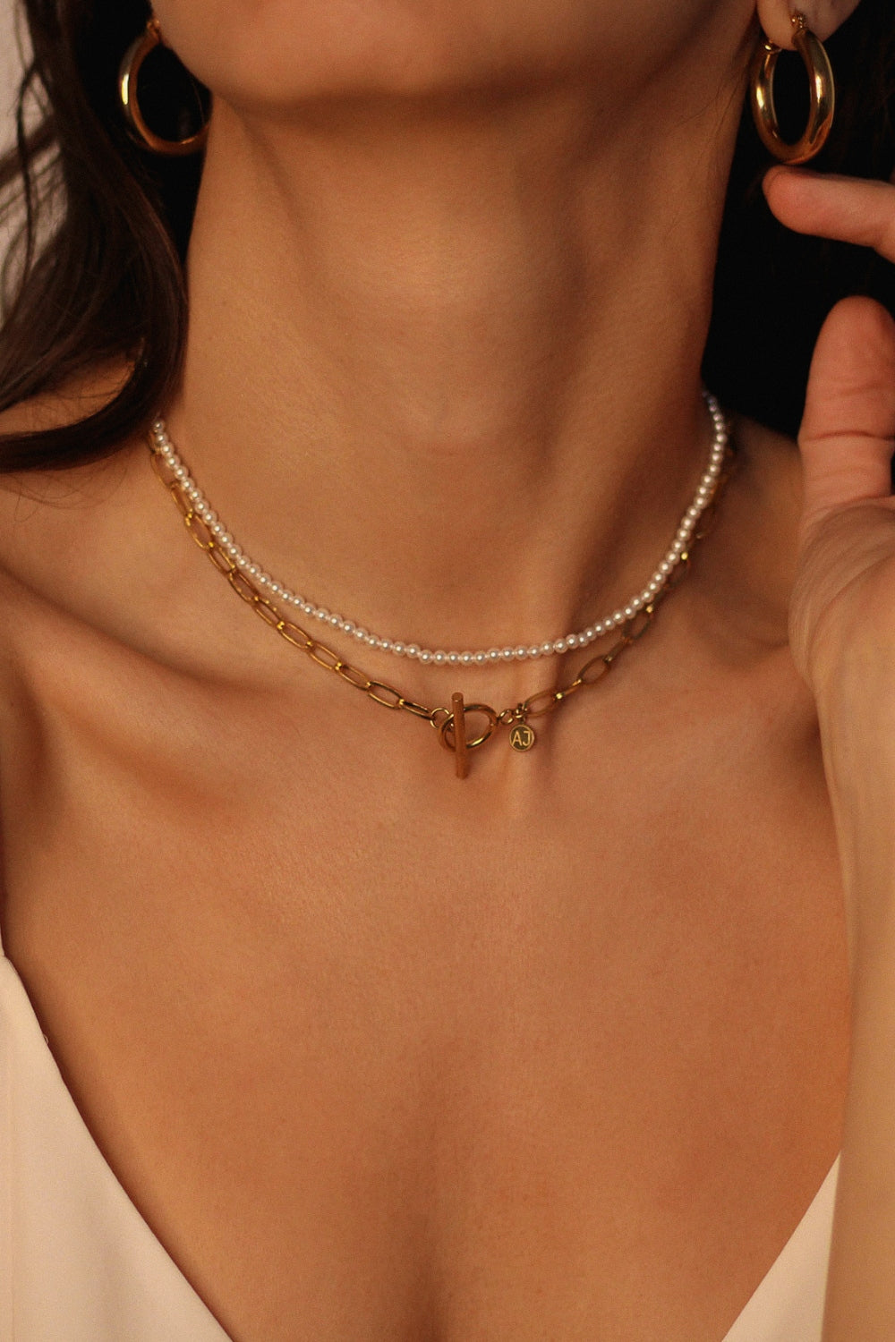 Waterproof 18k gold plated toggle choker. The set includes a sleek and minimalistic 18k gold plated toggle choker with a decorative gold ring and a bar that fits through it to secure the necklace. The choker is layered with a beaded pearl necklace, featuring lustrous white pearls strung on a delicate gold chain. The two necklaces complement each other perfectly, adding a touch of elegance and sophistication to the model's outfit