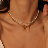 Waterproof 18k gold plated toggle choker. The set includes a sleek and minimalistic 18k gold plated toggle choker with a decorative gold ring and a bar that fits through it to secure the necklace. The choker is layered with a beaded pearl necklace, featuring lustrous white pearls strung on a delicate gold chain. The two necklaces complement each other perfectly, adding a touch of elegance and sophistication to the model's outfit