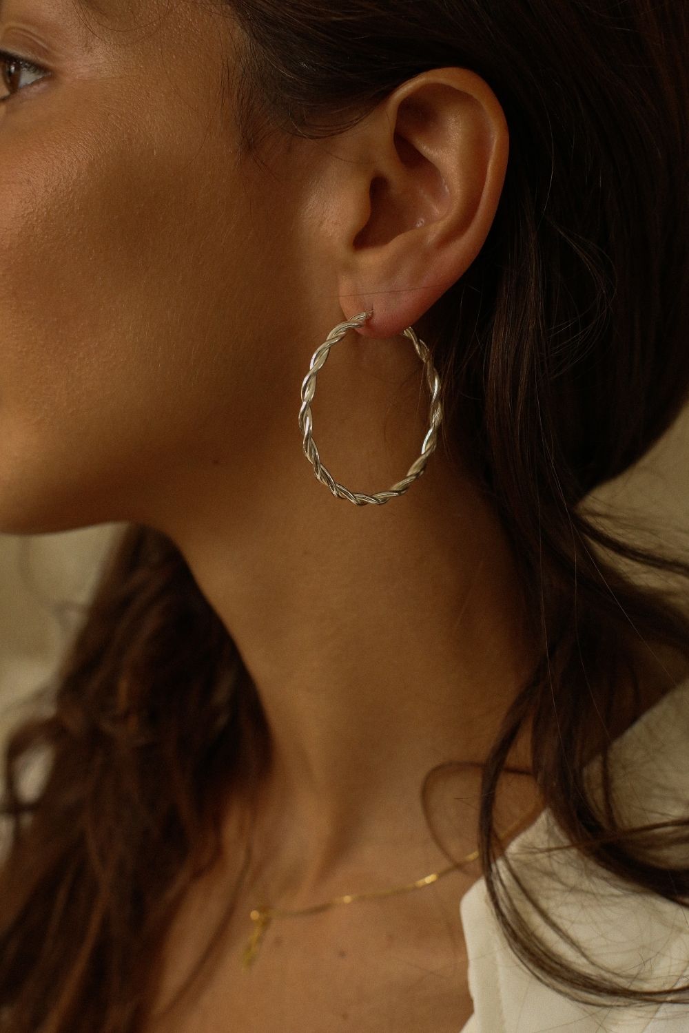 a pair of silver hoop earrings, featuring a twisted design. The hoops are large in size, yet lightweight, making them comfortable to wear. The silver has a polished finish, reflecting light and enhancing their shine. These striking earrings add a bold and elegant touch to any outfit.