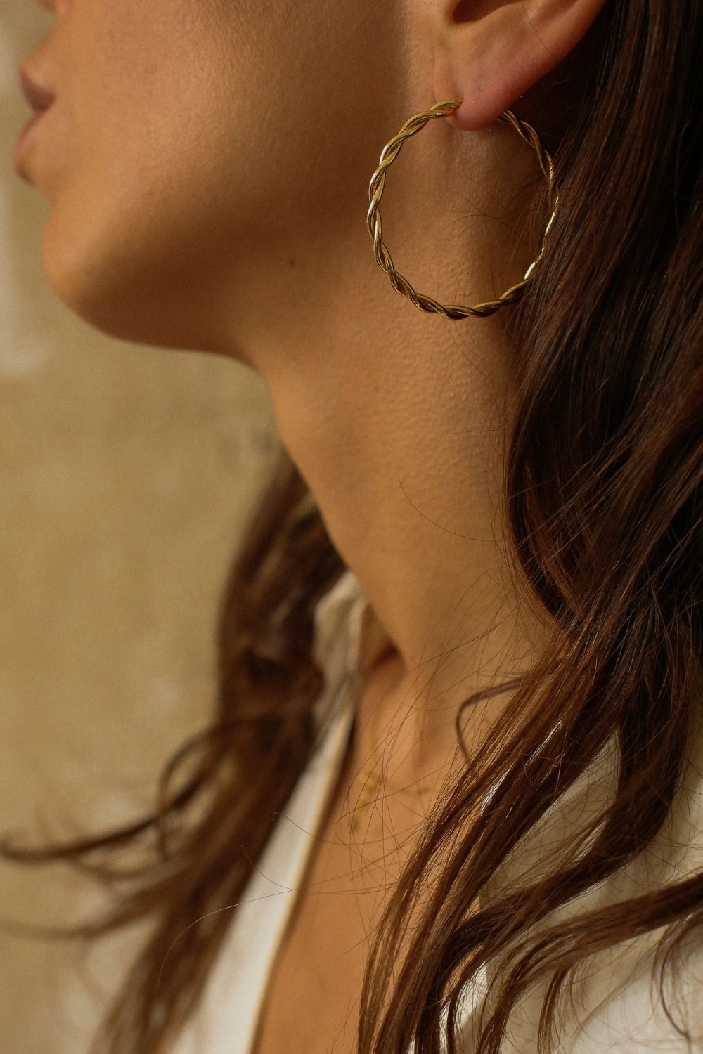 a pair of 18k gold vermeil hoop earrings, featuring a twisted design. The hoops are large in size, yet lightweight, making them comfortable to wear. The gold has a polished finish, reflecting light and enhancing their shine. These striking earrings add a bold and elegant touch to any outfit.