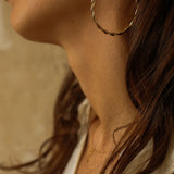 a pair of 18k gold vermeil hoop earrings, featuring a twisted design. The hoops are large in size, yet lightweight, making them comfortable to wear. The gold has a polished finish, reflecting light and enhancing their shine. These striking earrings add a bold and elegant touch to any outfit.