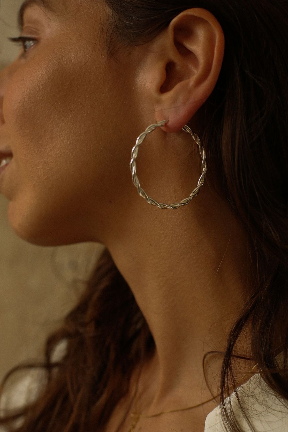 a pair of silver hoop earrings, featuring a twisted design. The hoops are large in size, yet lightweight, making them comfortable to wear. The silver has a polished finish, reflecting light and enhancing their shine. These striking earrings add a bold and elegant touch to any outfit.