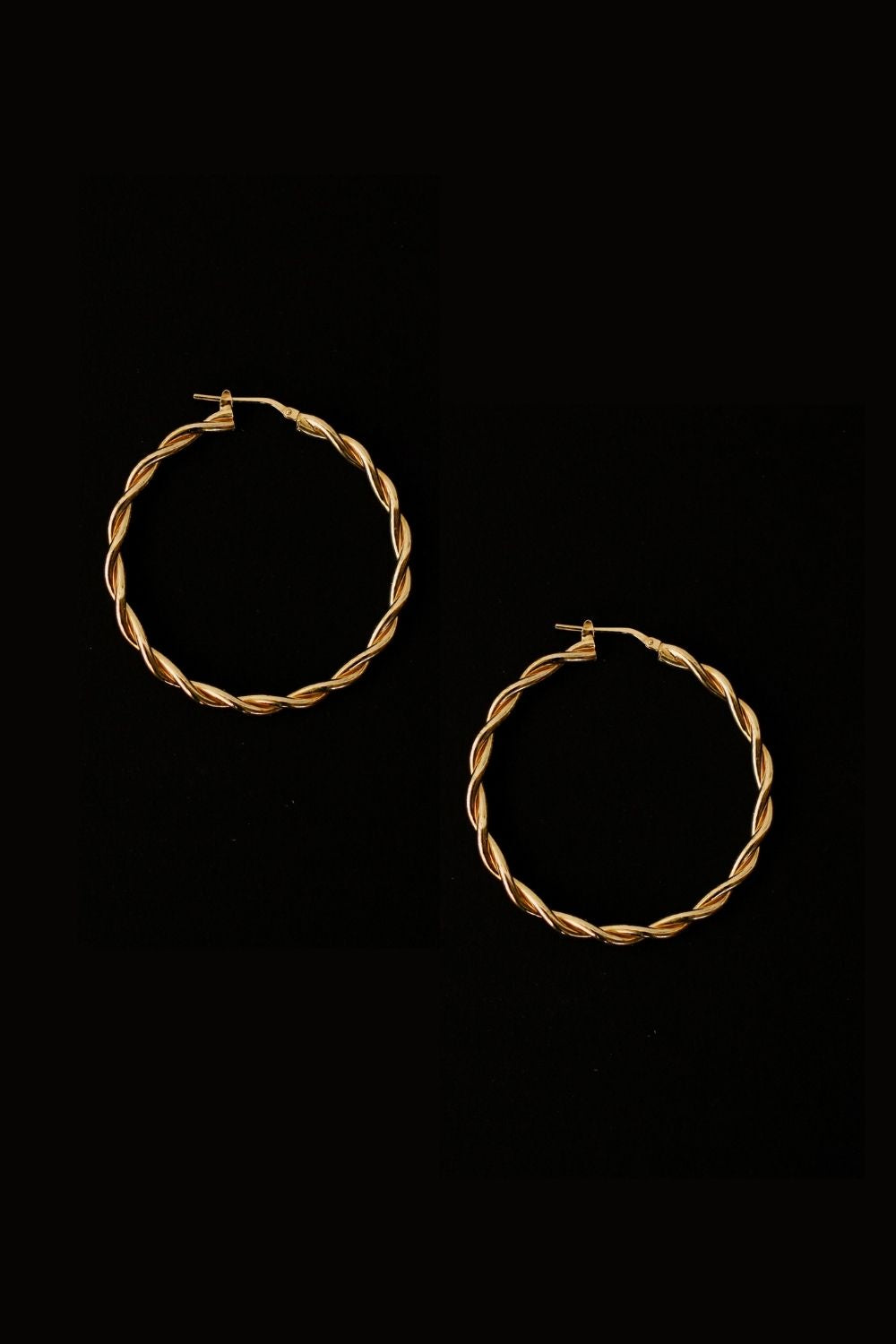 a pair of 18k gold vermeil hoop earrings, featuring a twisted design. The hoops are large in size, yet lightweight, making them comfortable to wear. The gold has a polished finish, reflecting light and enhancing their shine. These striking earrings add a bold and elegant touch to any outfit.