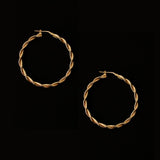 a pair of 18k gold vermeil hoop earrings, featuring a twisted design. The hoops are large in size, yet lightweight, making them comfortable to wear. The gold has a polished finish, reflecting light and enhancing their shine. These striking earrings add a bold and elegant touch to any outfit.