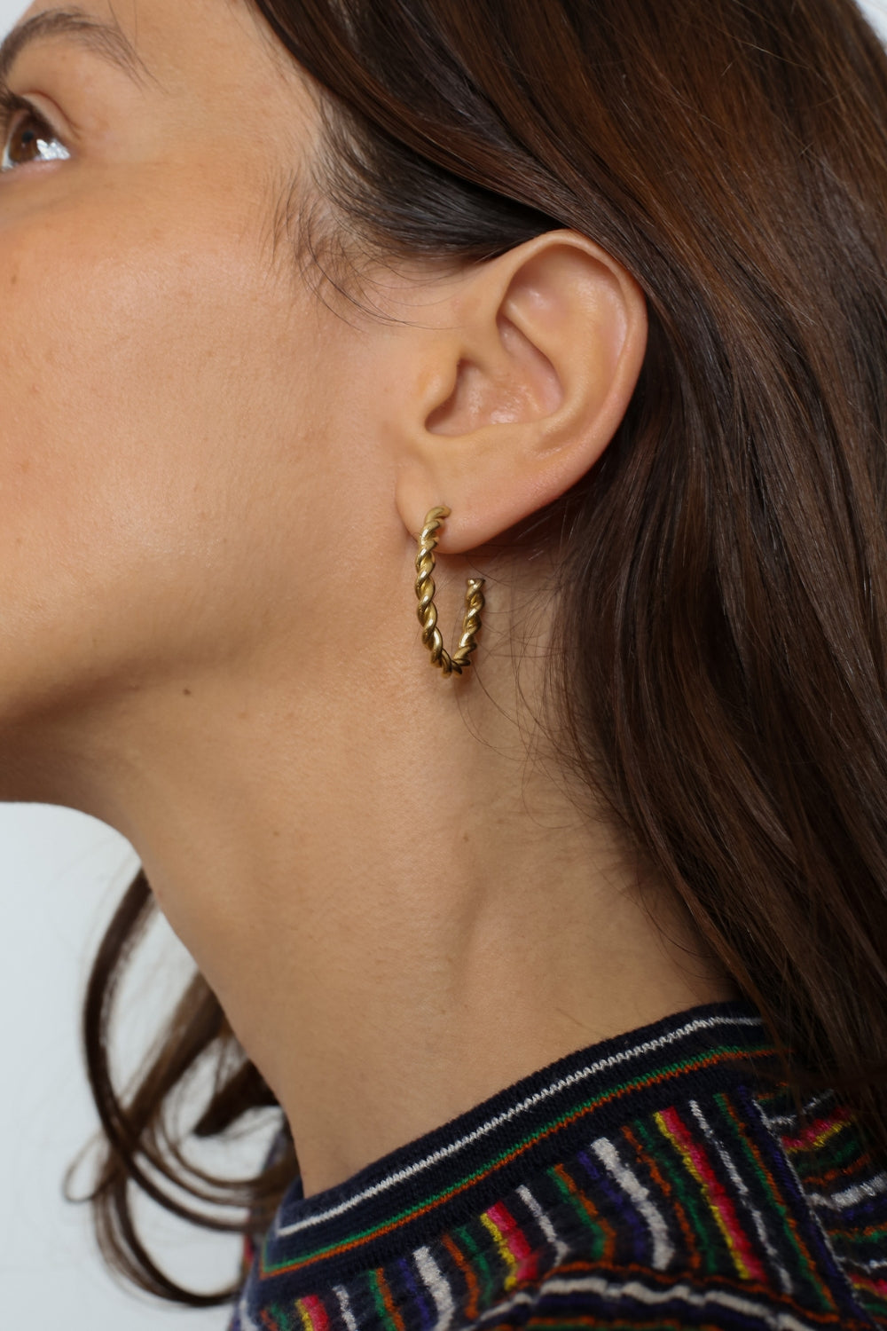 Twisted hoops in 18k gold plated. The earrings feature a unique and eye-catching twisted design. The gold plated material adds a touch of luxury and elegance. These hoops have a polished finish that enhances their shine.