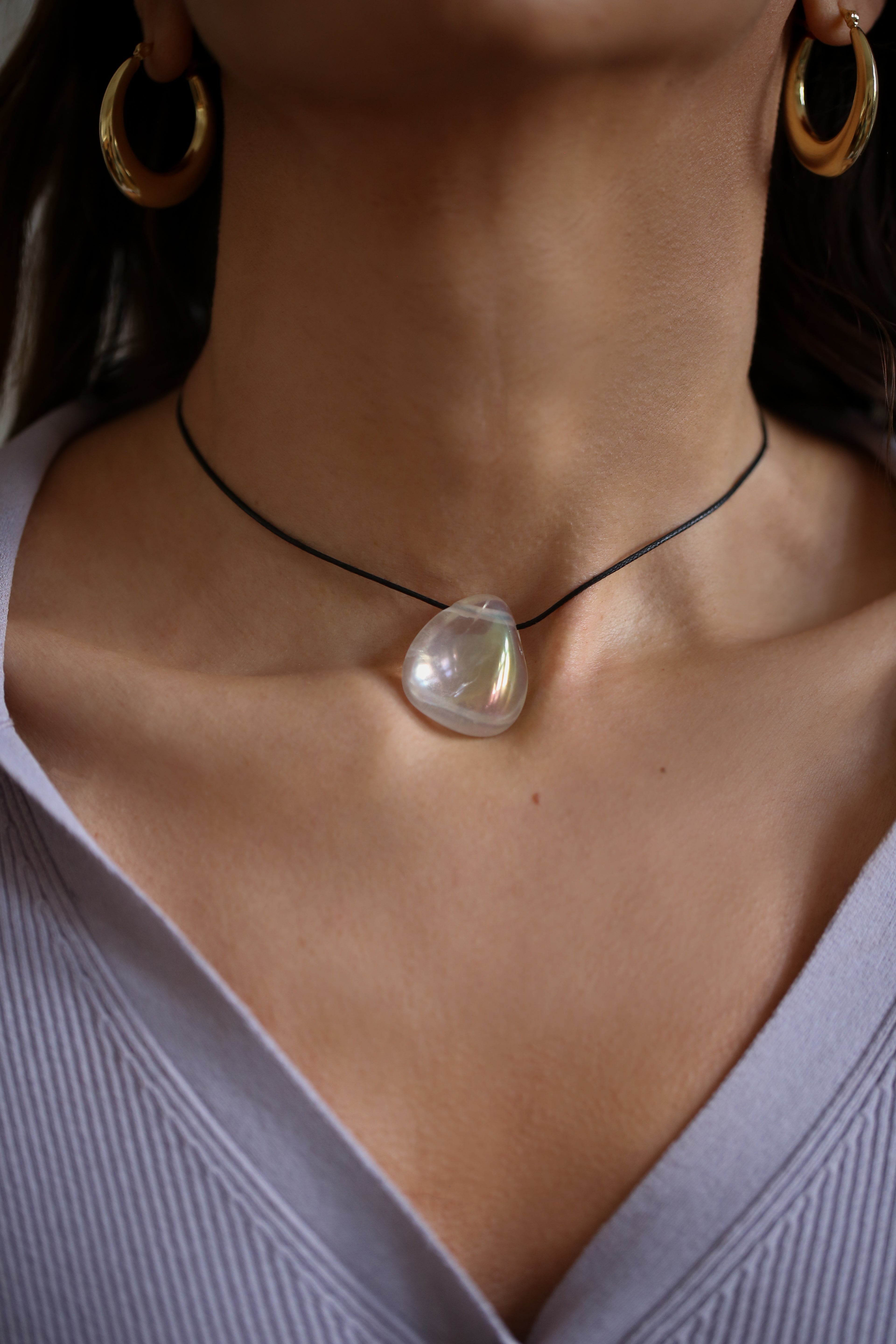 A person wearing a angel aura quartz stone necklace with an adjustable black cord.