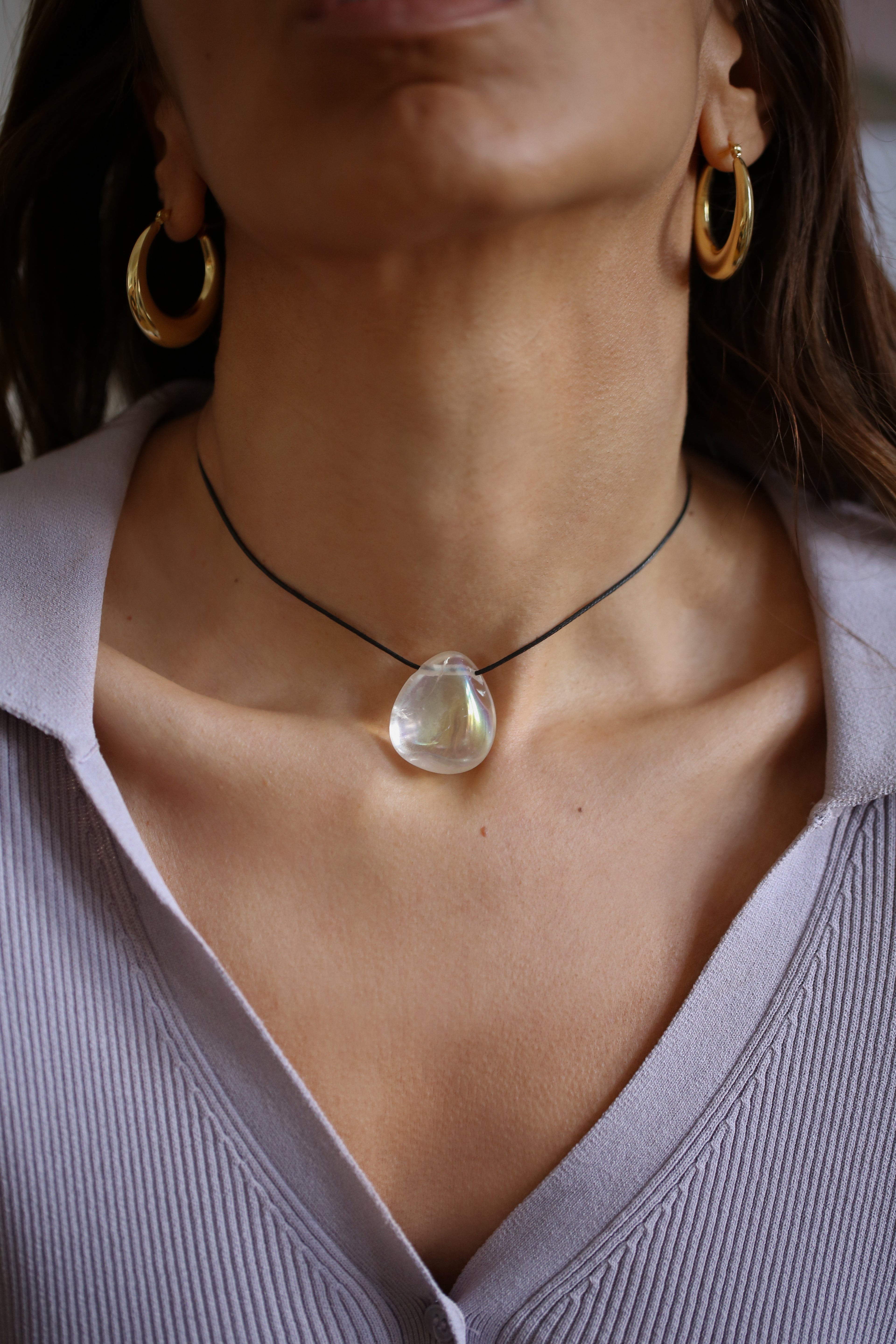 A person wearing a angel aura quartz stone necklace with an adjustable black cord.