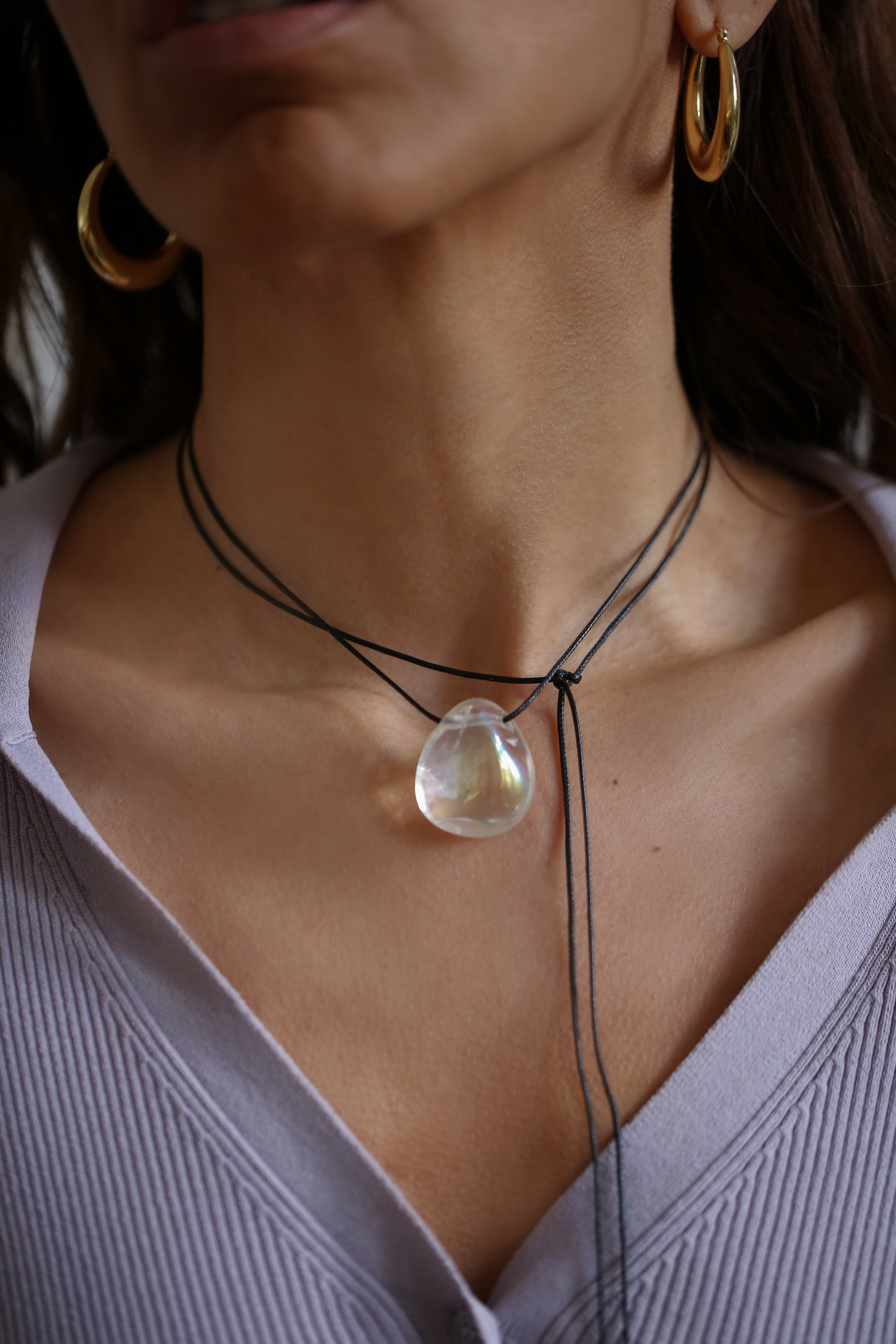 A person wearing a angel aura quartz stone necklace with an adjustable black cord.