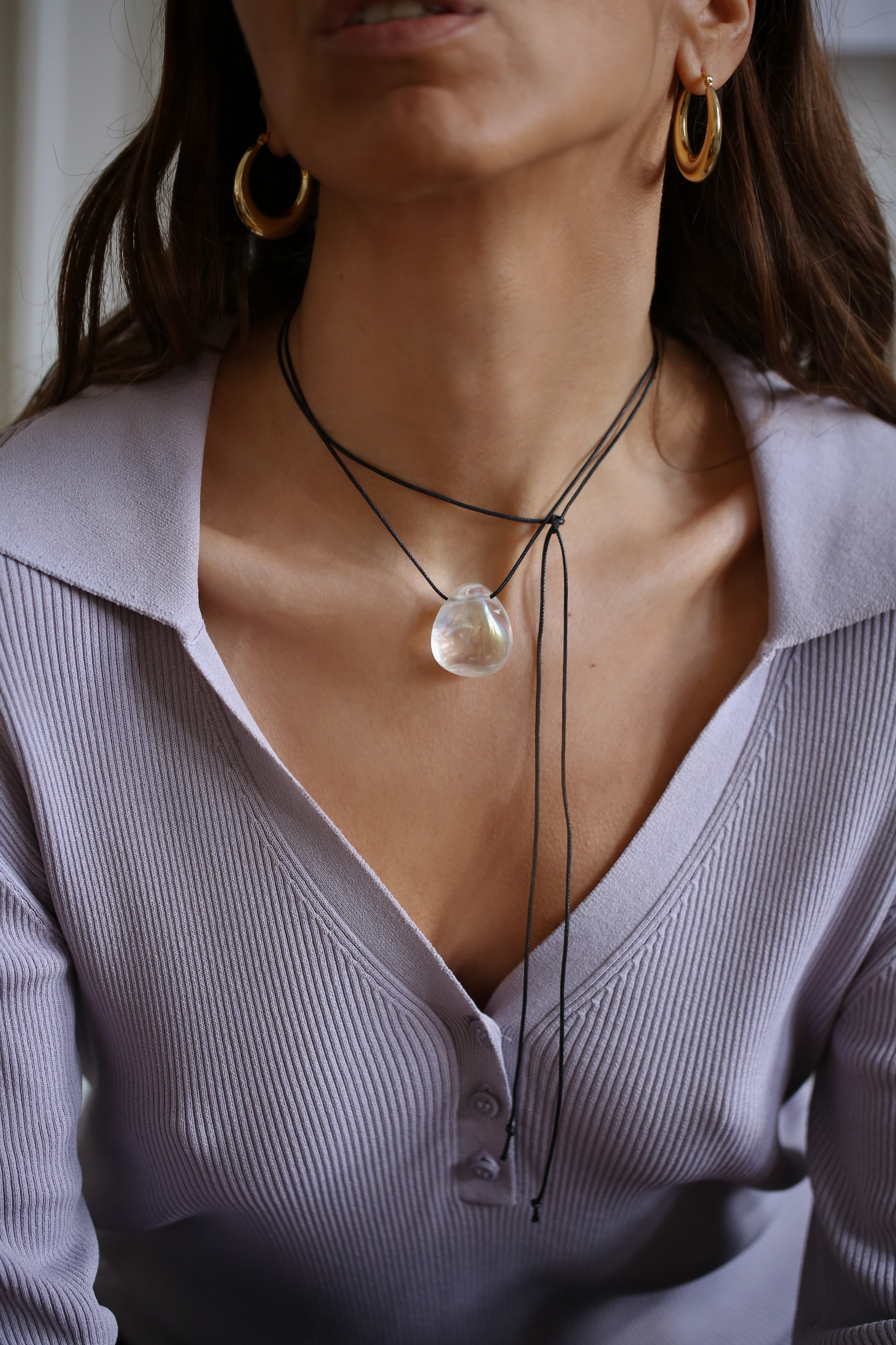 A person wearing a angel aura quartz stone necklace with an adjustable black cord.