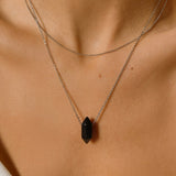 Black obsidian crystal necklace. The necklace features a pointed black obsidian crystal pendant attached to a gold chain, creating a stunning and eye-catching piece of jewelry.