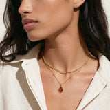 Woman wearing a gold necklace with a pendant against a neutral background