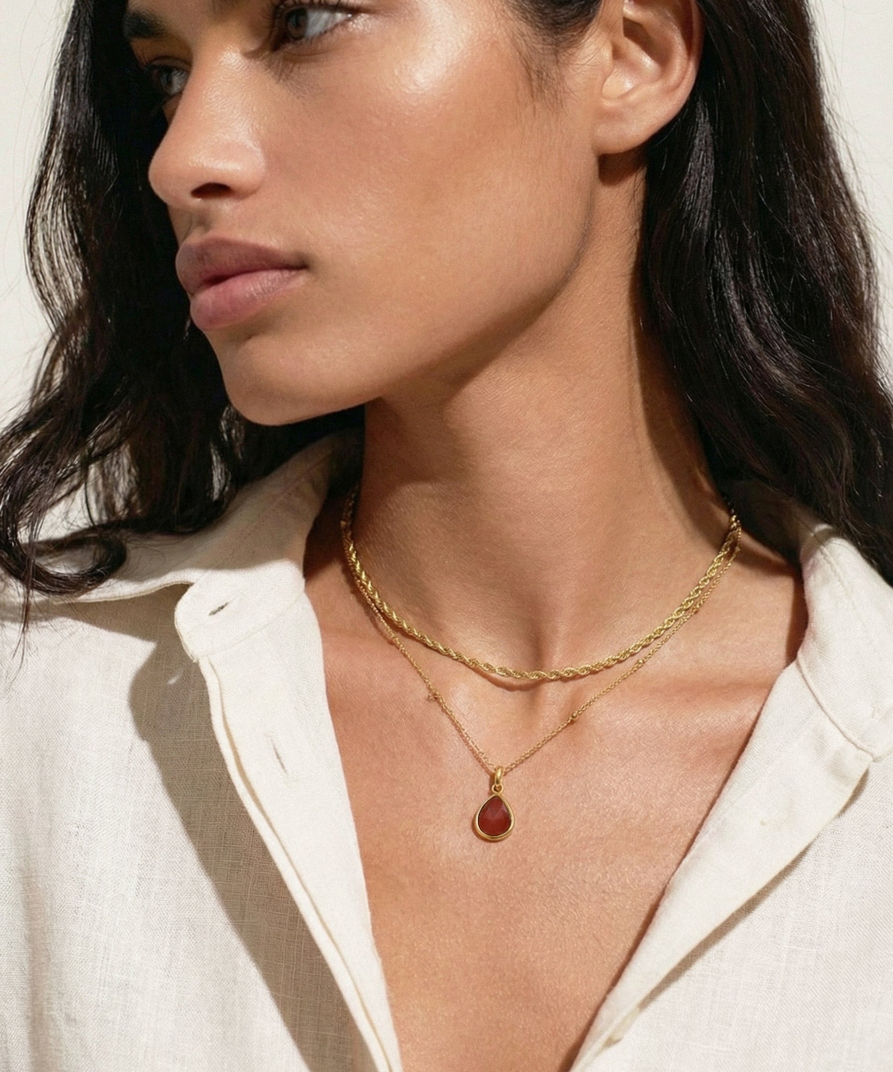 Woman wearing a gold necklace with a pendant against a neutral background