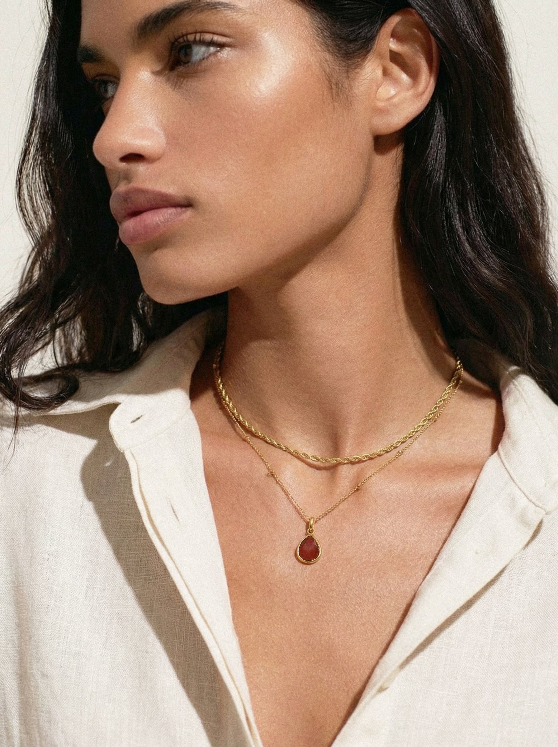Woman wearing a gold necklace with a pendant against a neutral background