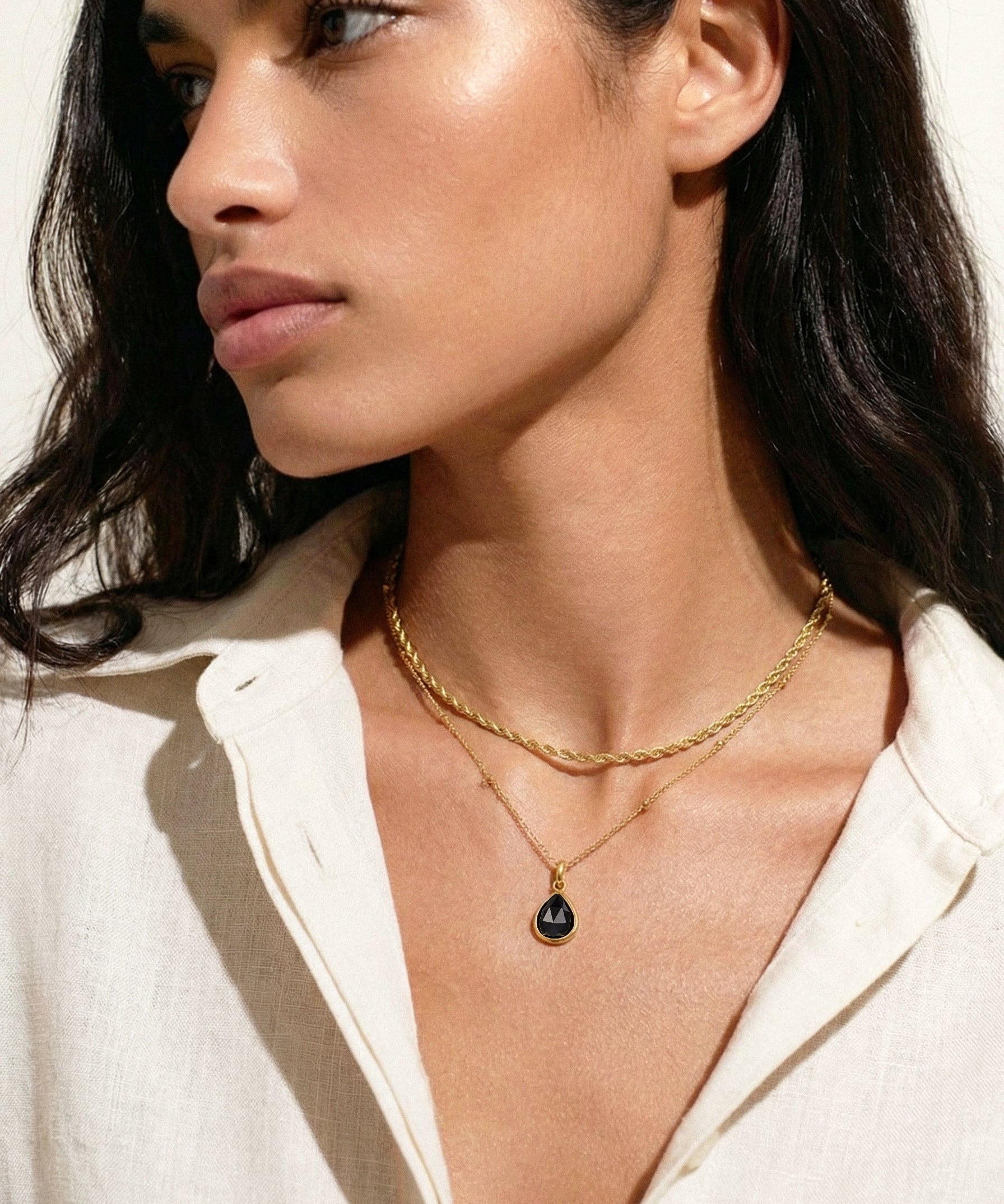 Woman wearing a gold necklace with a black pendant against a neutral background
