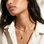 Woman wearing a gold necklace with a labradorite pendant, looking off to the side.