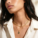 Woman wearing a gold necklace with a labradorite pendant, looking off to the side.