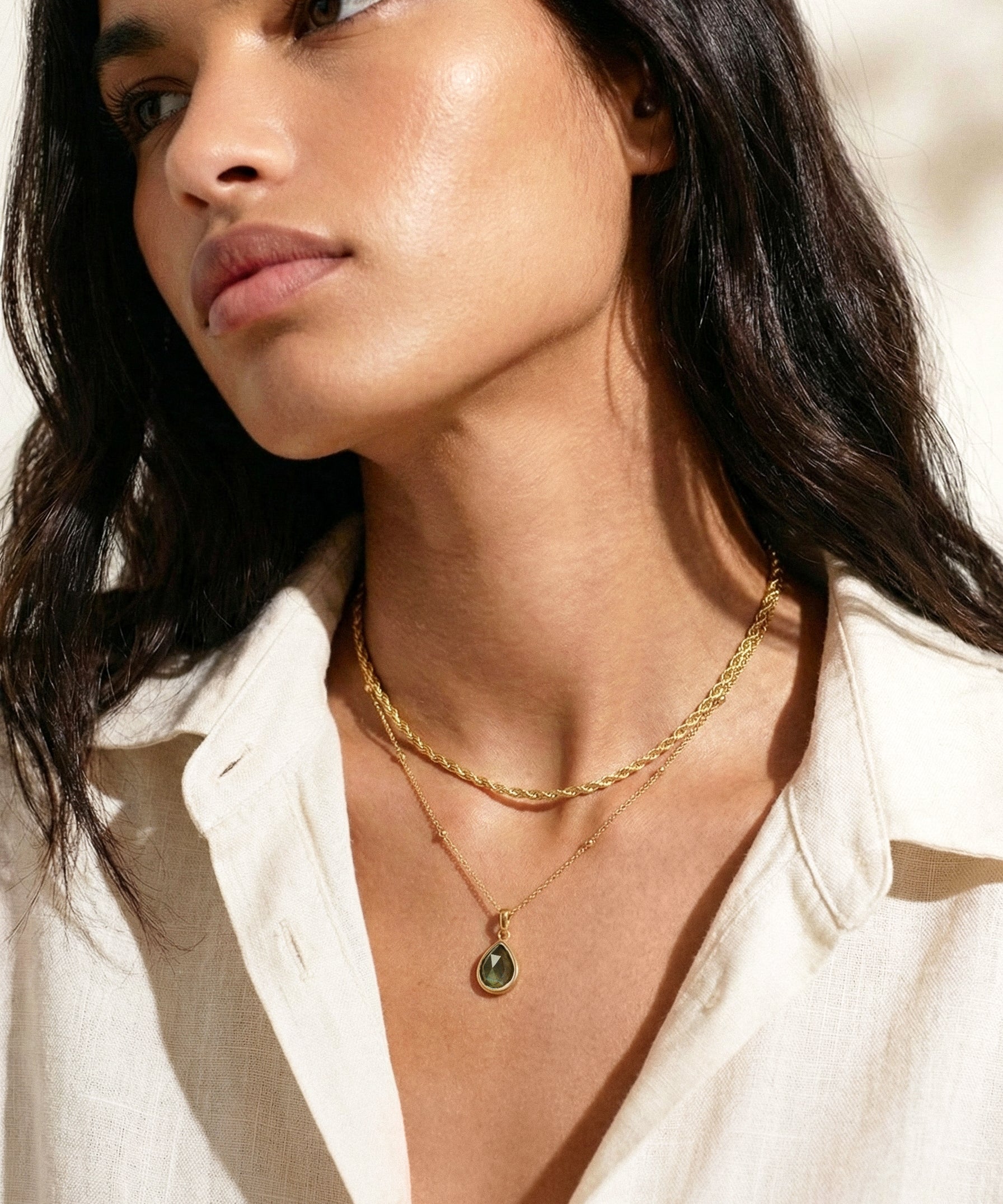 Woman wearing a gold necklace with a labradorite pendant, looking off to the side.