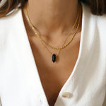 A person wearing a gold rope necklace with a white sweater and a neutral facial expression.