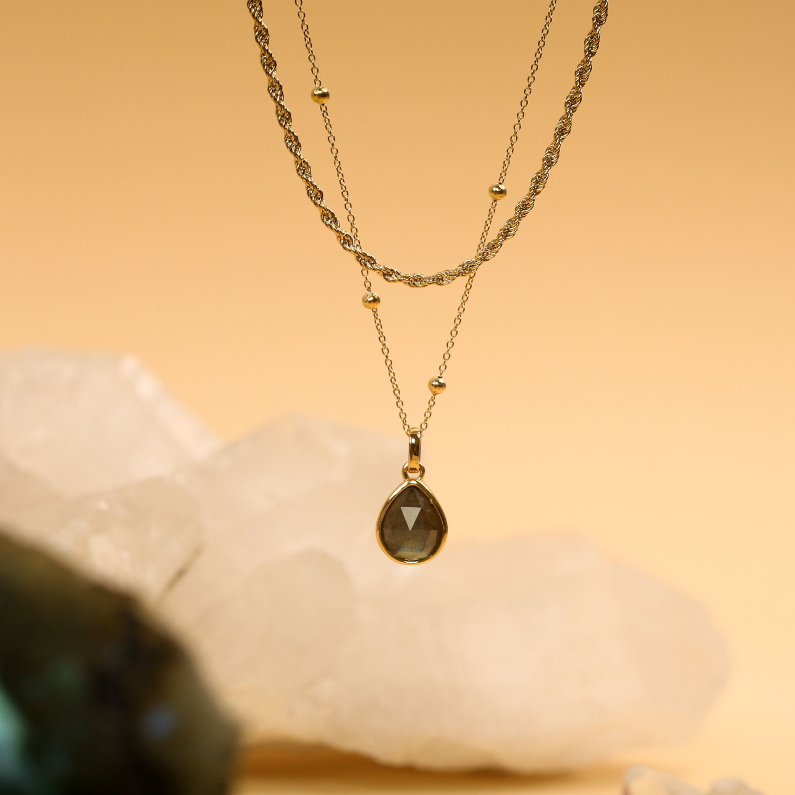 Gold necklace with a teardrop pendant on a stone background