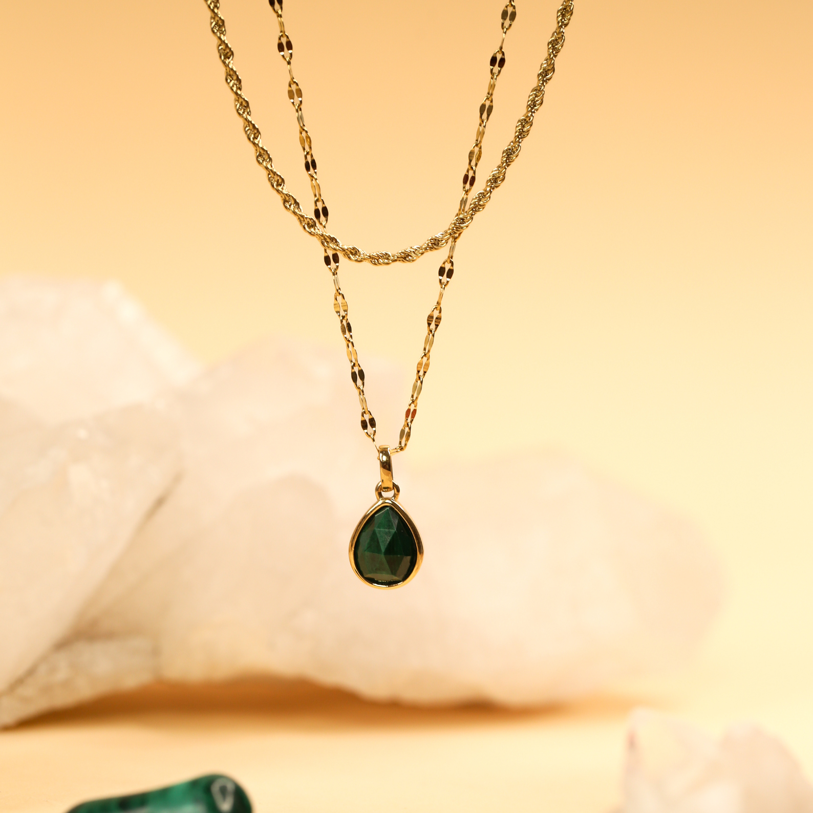 Gold necklace with a green teardrop pendant on a soft beige background