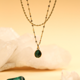 Gold necklace with a green teardrop pendant on a soft beige background
